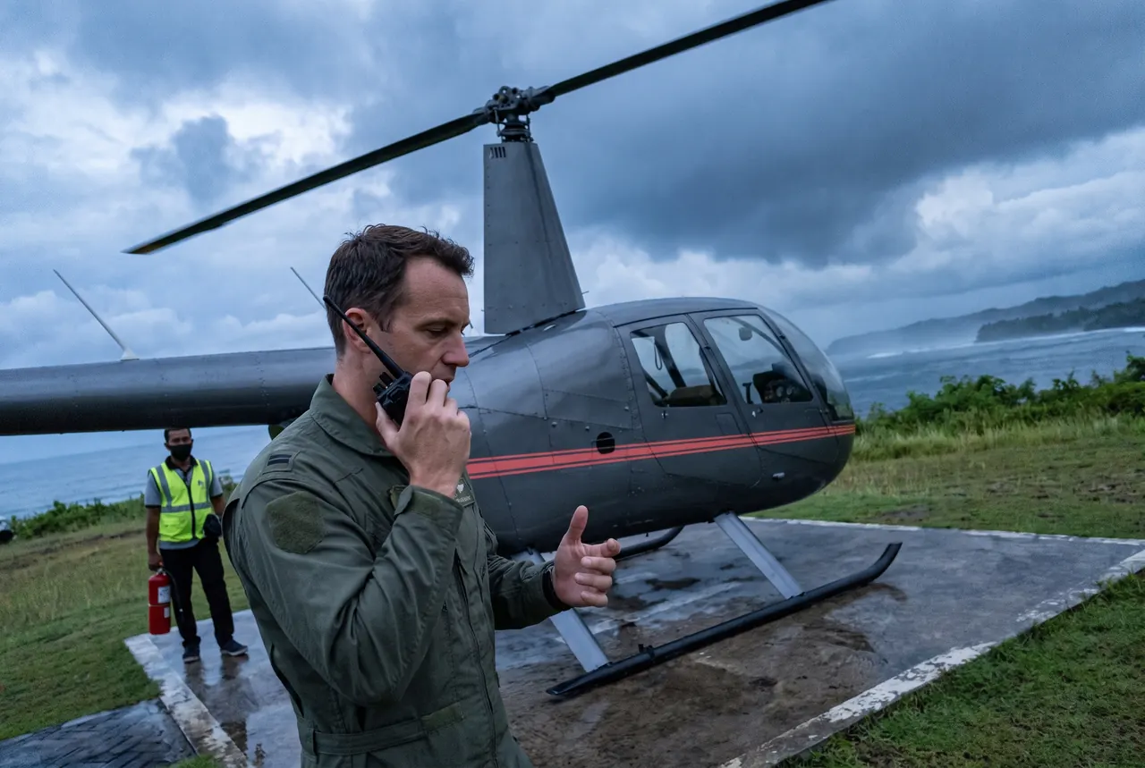 Pilot on the radio beside a helicopter at dawn, ready for an urgent flight in Bali